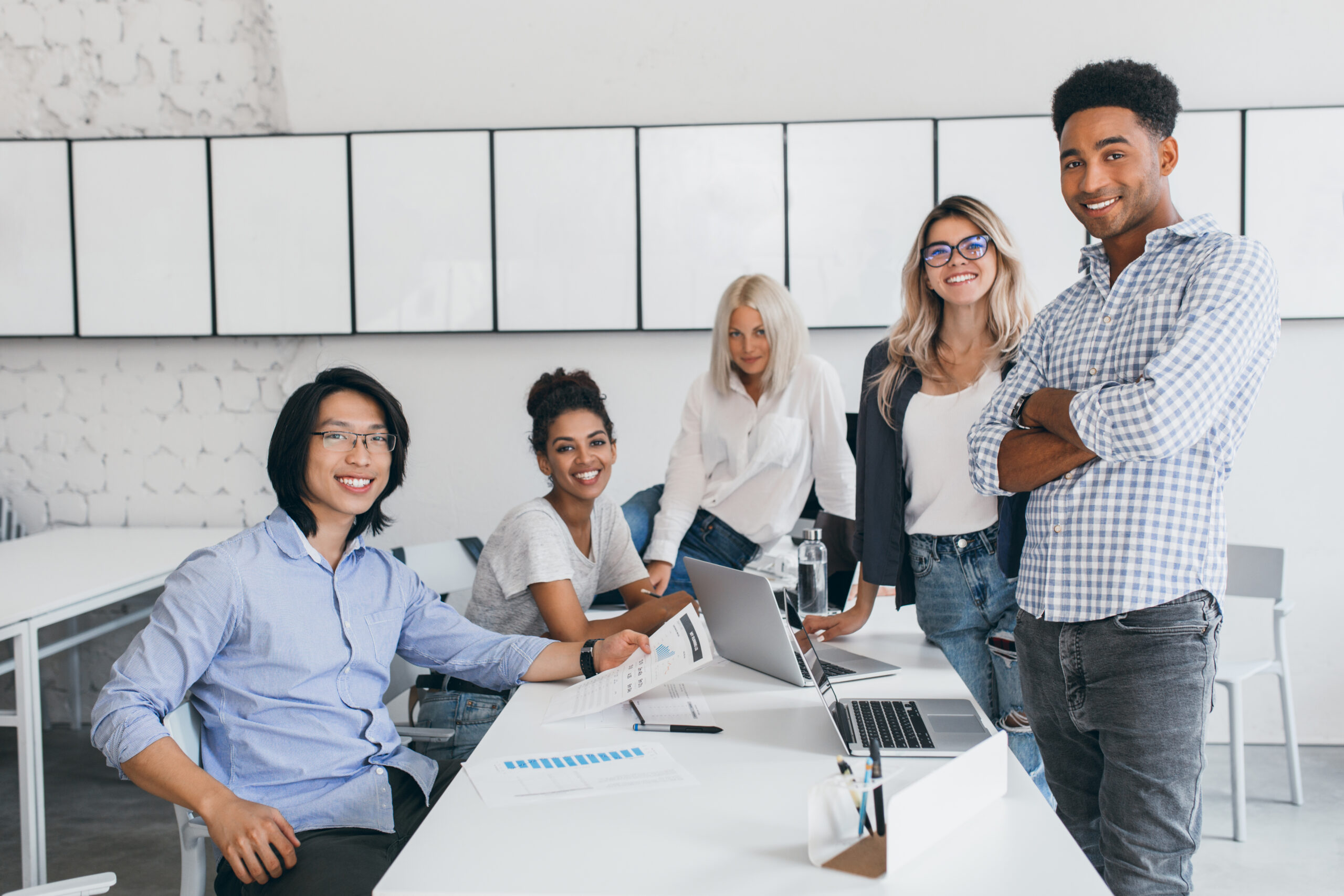 Smiling young web-developers posing around table with laptops on it. Indoor portrait of asian student with black hair spending time with friends in university.. Clinical Trial Research